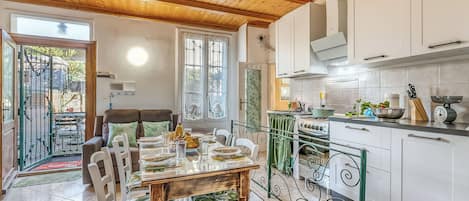 Une cuisine moderne avec des meubles blancs, une rambarde en métal vert et un coin repas comprenant une table et des chaises en bois.
