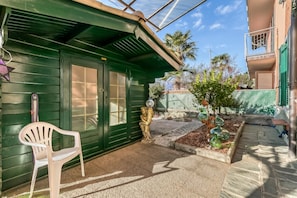 A green building with a door and windows, a small garden with a tree and decorative vases, and a white plastic chair. - Butterfly Apartment: Lake Maggiore Luino Apartment With Balcony (Luino)