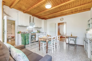 A spacious living area with a wooden ceiling, a dining table with chairs, a sofa, and a kitchen in the background. - Butterfly Apartment: Lake Maggiore Luino Apartment With Balcony (Luino)
