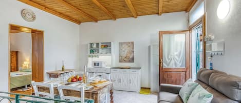 Uma sala de estar aconchegante com teto de madeira, uma mesa de jantar com cadeiras, um sofá com almofadas, uma área de cozinha com armários, e uma pequena mesa de jantar com comida e bebidas.