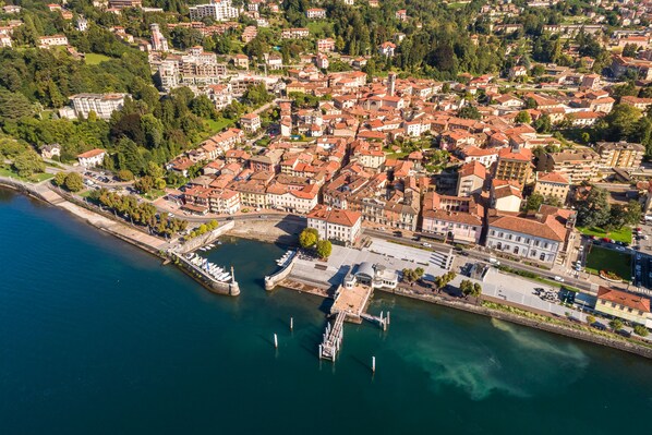 An aerial view of a coastal town with a marina, buildings with red-tiled roofs, and a mix of residential and commercial structures. - Butterfly Apartment: Lake Maggiore Luino Apartment With Balcony (Luino)