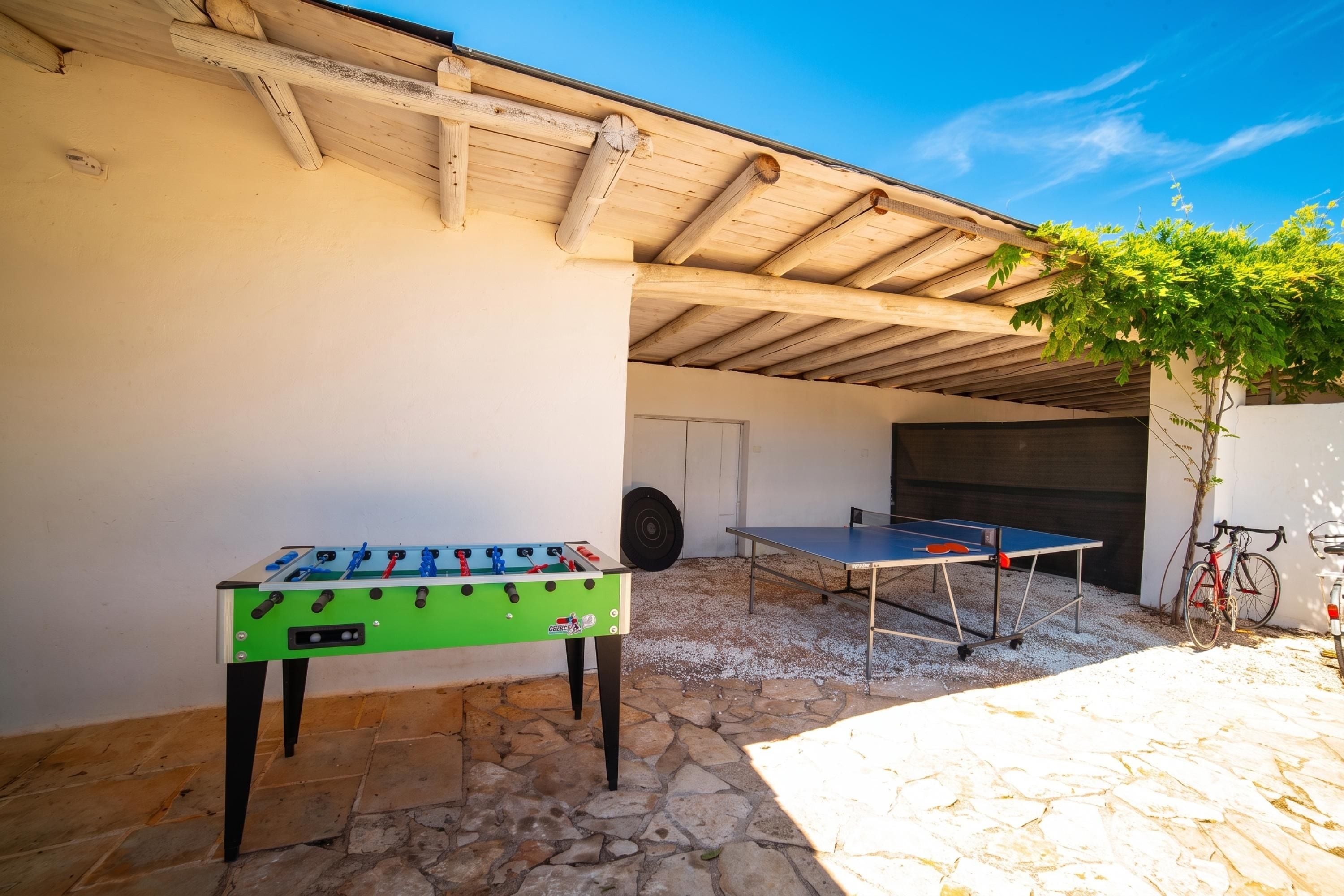 An outdoor patio with a foosball table, a ping pong table, and a bicycle.