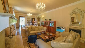 Uma sala de estar ampla com um sofá, mesa de centro e televisão. Há uma lareira e um candelabro.