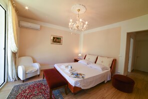 A bedroom with a large bed, a bedside table, a chair, a red ottoman, a chandelier, and a patterned rug. - Villa Nina - Luxury Villa With Pool in Salento (Zollino)