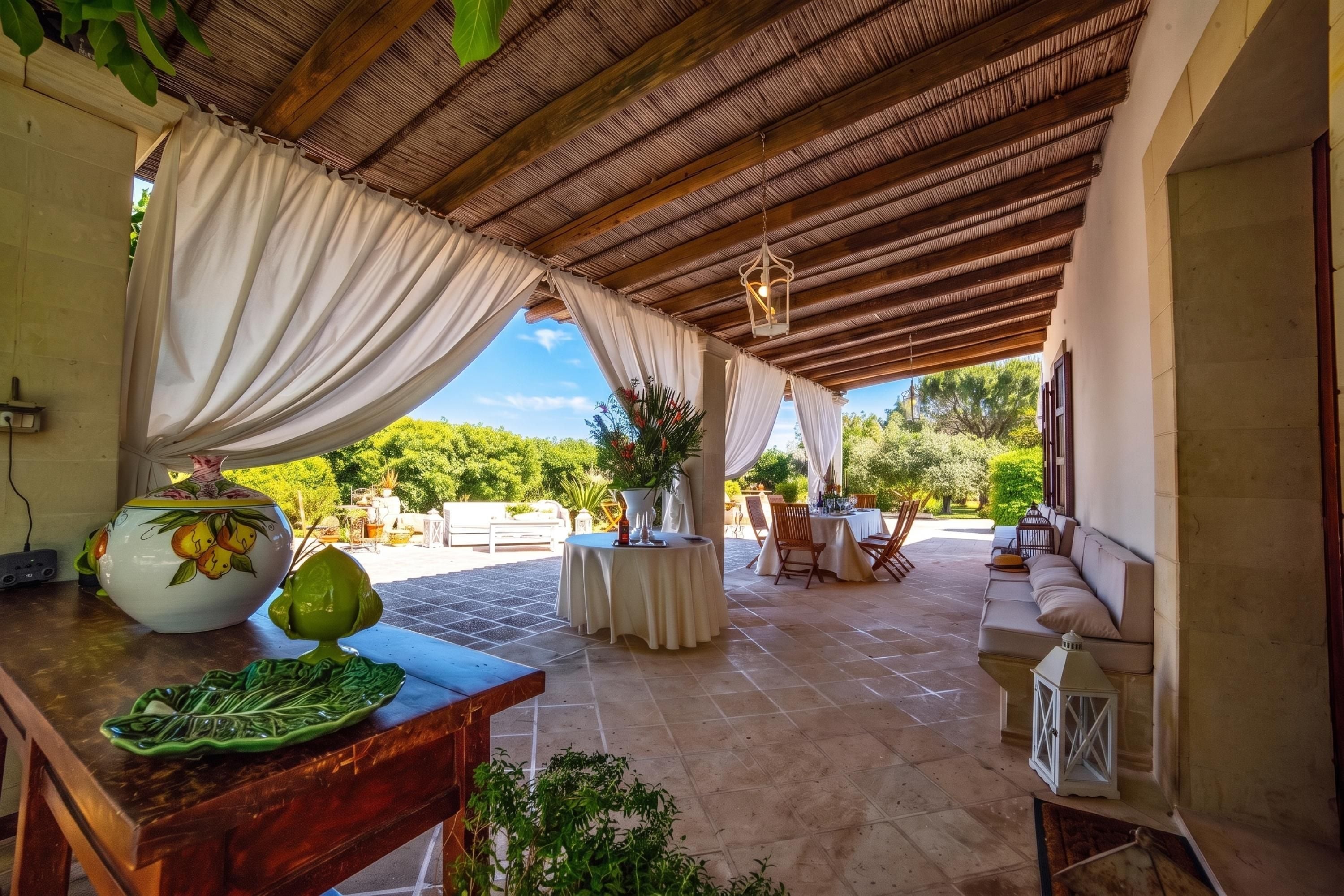 Patio esterno con zona salotto coperta, tavolo con un vaso e una ciotola, e vista su piante.