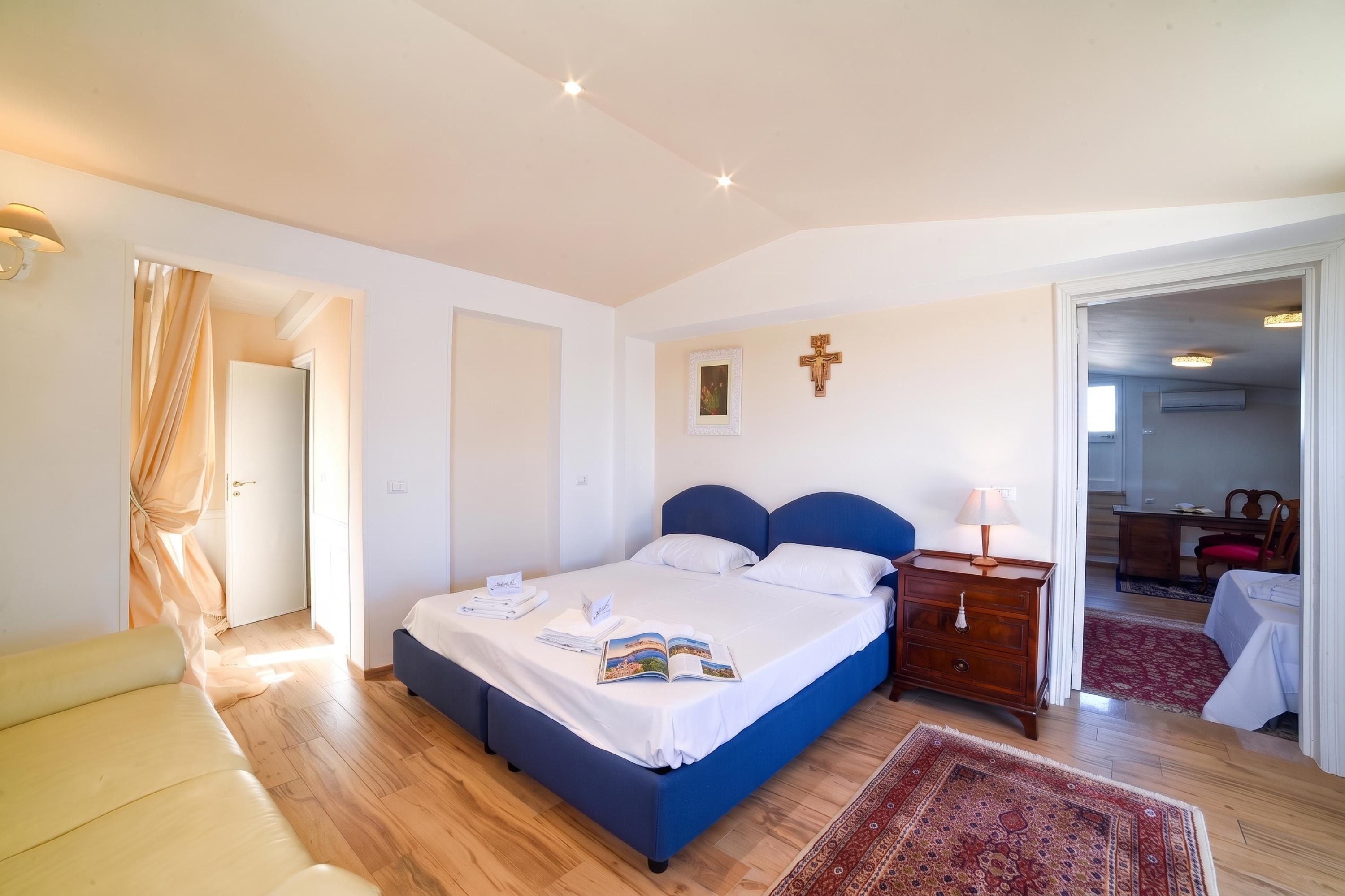 A bedroom with a bed, bedside table, lamp, and a door leading to another room.