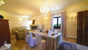Uma sala de jantar com uma mesa posta para quatro pessoas, um candelabro, um sofá e uma lareira.