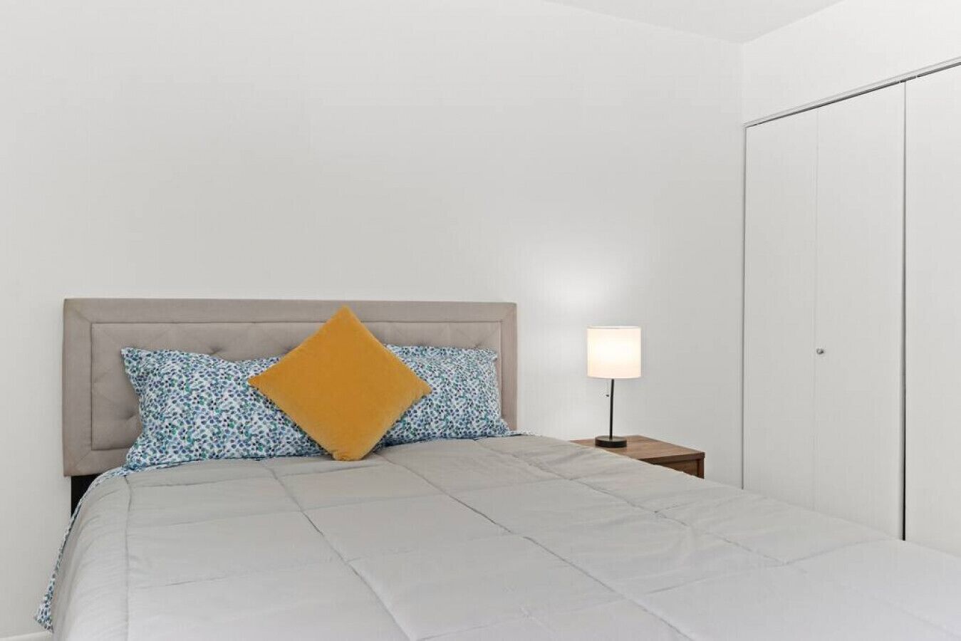 Een slaapkamer met een bed, een nachtkastje met een lamp en een kledingkast.