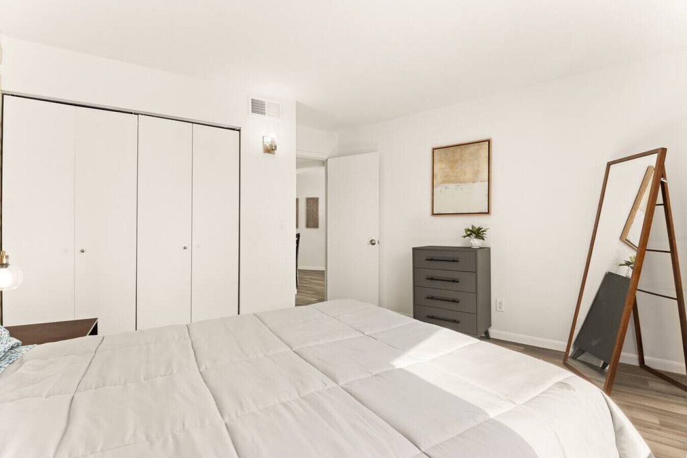 A bedroom with a large bed, a wardrobe, a dresser, a mirror, and a painting on the wall.