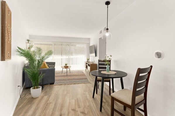 Un salon moderne avec un canapé, une table à manger et des chaises, une plante en pot et un téléviseur fixé au mur.
