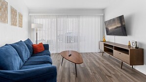 Una sala de estar moderna con un sofá azul, una mesa de centro de madera y un televisor en la pared.