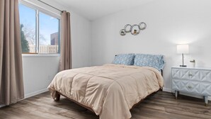 Un dormitorio con cama, mesita de noche, lámpara y ventana con cortinas.