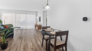 Un moderno comedor con suelo de madera, una mesa redonda y sillas. Hay una lámpara colgante sobre la mesa y un televisor montado en la pared.