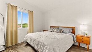A bedroom with a bed, a nightstand, a lamp, and a window with curtains. - Concord C1 · Slice of the Good Life: Concord C1 (Peoria)