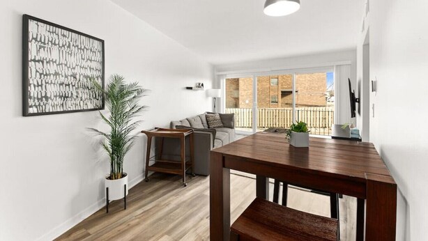 Eine moderne Wohnung mit Essbereich, einer Sofagarnitur, einer großen Pflanze und einem Balkon mit Stadtblick.