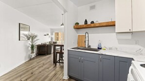 Eine moderne Küche mit grauen Schränken, einer Marmorarbeitsplatte und einem Essbereich aus Holz.