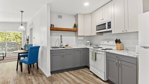A modern kitchen with grey cabinets, a white refrigerator, a microwave, and a stove. There is a dining area with a blue chair and a table. - Concord C6 · Slice of the Good Life: Concord C6 (Peoria)