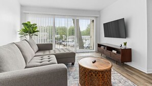 Un soggiorno moderno con un divano modulare grigio, un tavolino in legno, una TV a parete e una porta scorrevole in vetro che dà su un balcone.