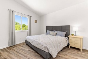 Ett sovrum med en säng, ett nattduksbord, en lampa och ett fönster med gardiner.