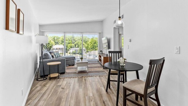 Ein modernes Wohnzimmer mit einer Couch, Sesseln, einem Couchtisch und einem Esstisch. Ein großes Fenster bietet Blick auf Grünflächen.