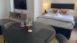 Una habitación de hotel con cama, mesita de noche, lámpara y televisor montado en la pared.