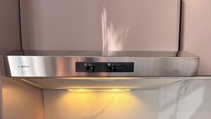 Una cocina con un fogón de inducción Bosch, una cafetera Kenwood y una campana extractora de acero inoxidable.