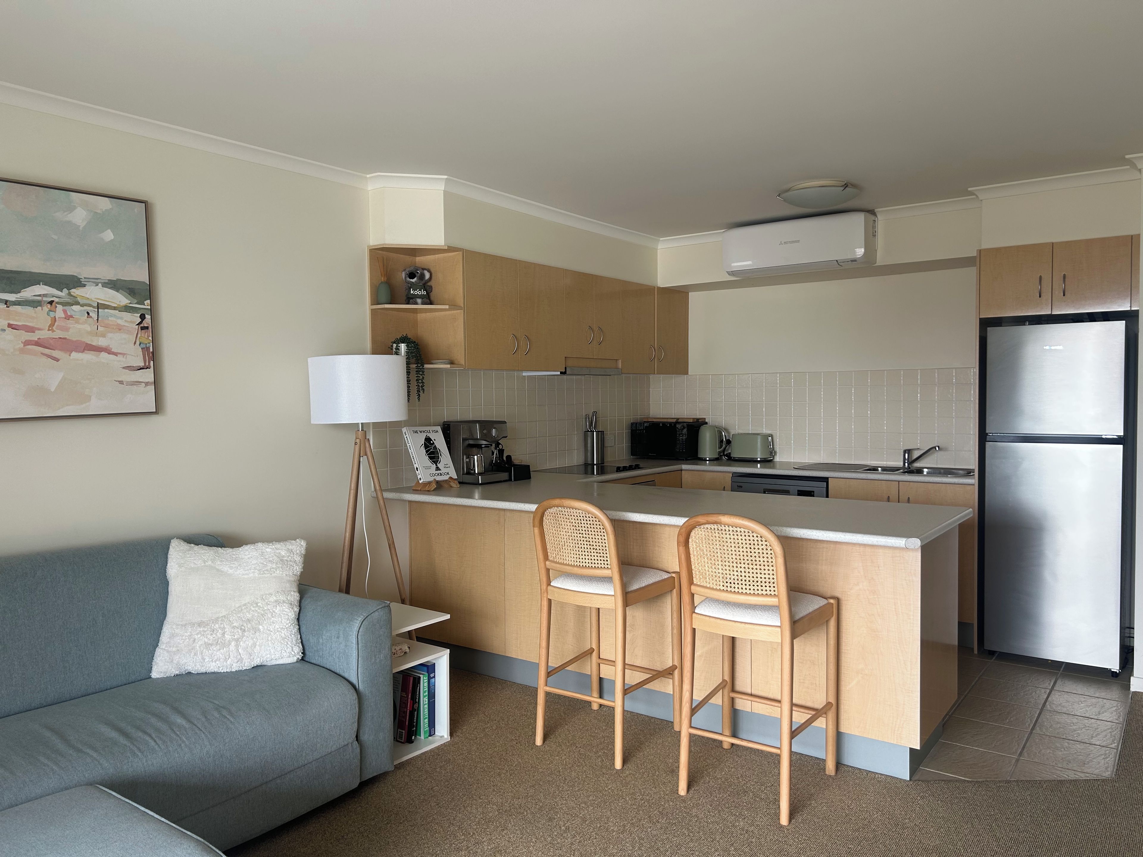 A compact kitchen with a central island, a sofa with a white cushion, and a lamp.