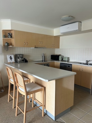 A modern kitchen with a central island, bar stools, a coffee machine, a microwave, and a toaster.