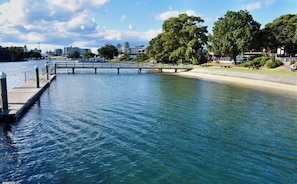 A waterfront park with a bridge, benches, and picnic tables.