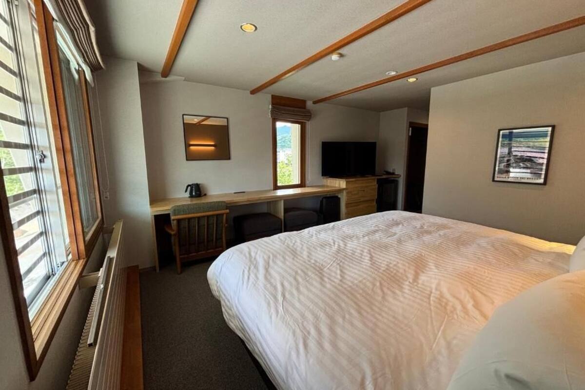 Habitación de hotel con una cama grande, un escritorio con silla, un televisor y una ventana con persianas.