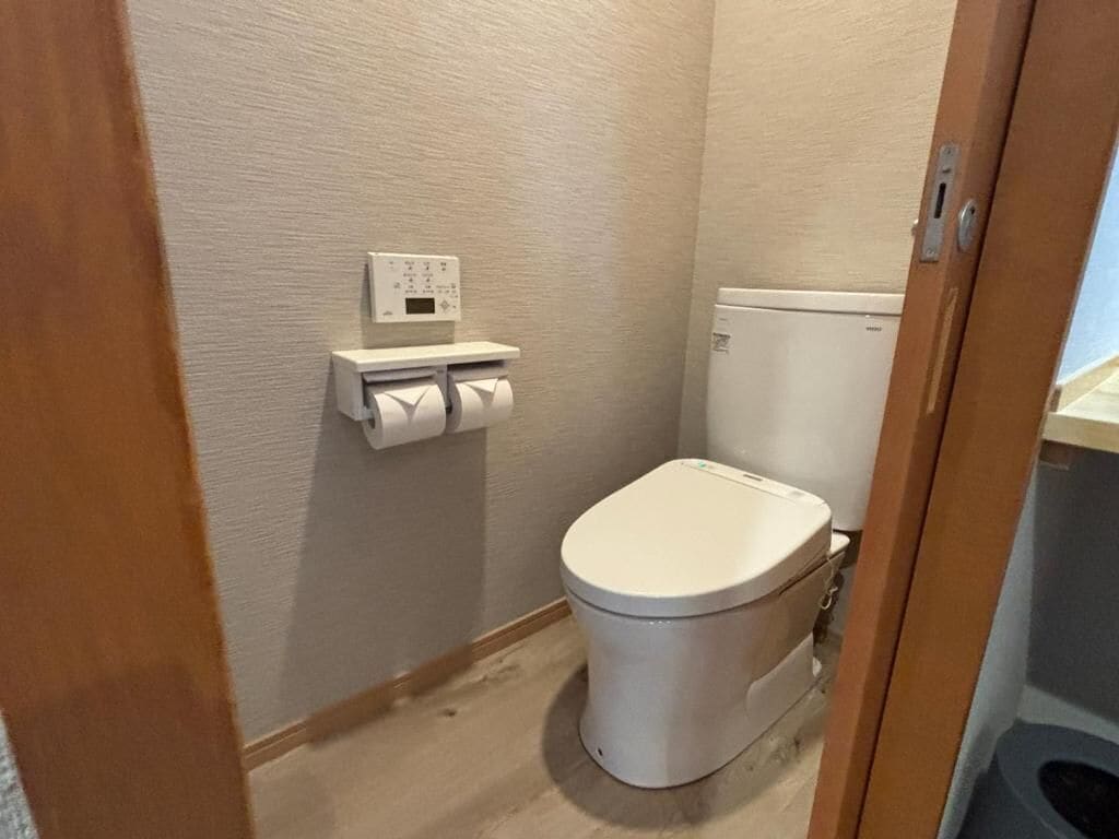 A small, compact bathroom with a toilet, a wall-mounted toilet paper holder, and a visible electrical outlet.