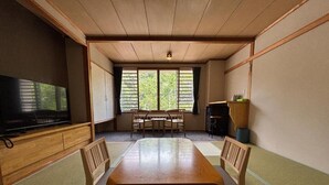 Ein traditioneller japanischer Raum mit Tatami-Bodenbelag, einem niedrigen Holztisch und einem Fernseher auf einem Schrank.