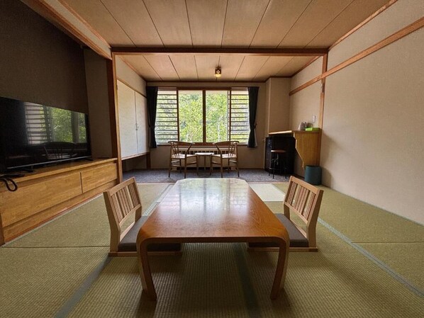 A traditional Japanese room with tatami flooring, a low wooden table, and a television on a cabinet.