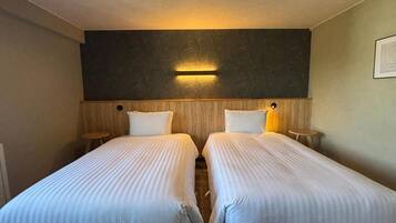 A hotel room with two single beds, a dark textured wall, and a wall-mounted light fixture.