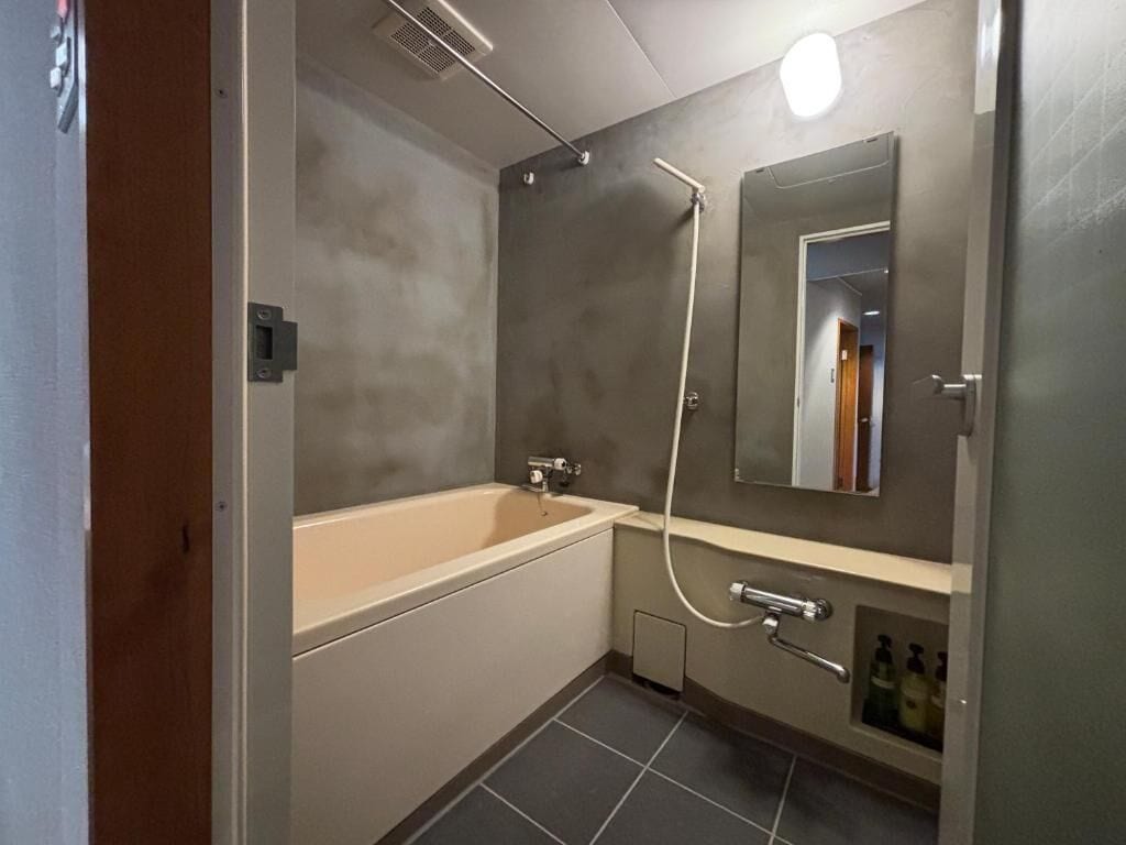 Une salle de bain moderne équipée d’une baignoire, d’une douche, d’un miroir et d’une étagère où sont rangés les articles de toilette.