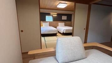 A hotel room with a single bed, a small seating area, and a view of another room with two beds.