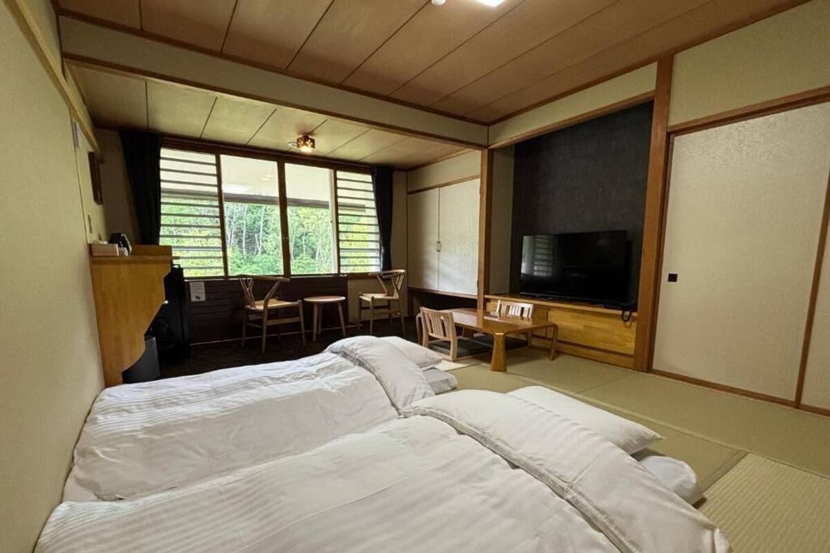 Habitación de hotel con dos camas, un escritorio, una silla, un televisor y un ventanal grande.