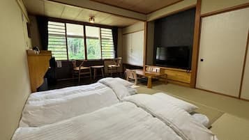 Quarto de hotel com duas camas, uma escrivaninha, uma cadeira, uma televisão e uma janela grande.