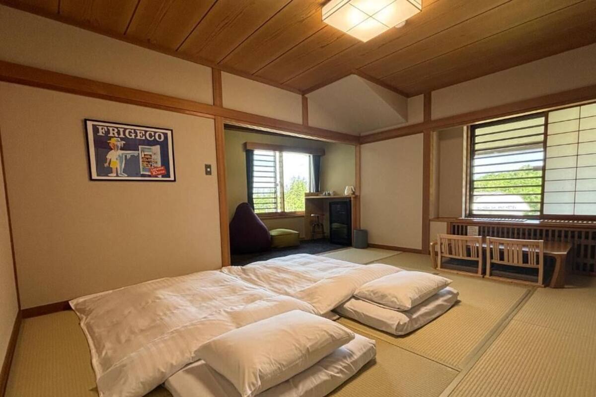 Una habitación japonesa tradicional con suelo de tatami, una futón, un banco futón y una pequeña mesa.