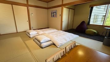 A traditional Japanese room with tatami flooring, a futon bed, a wooden table, and a window with blinds.