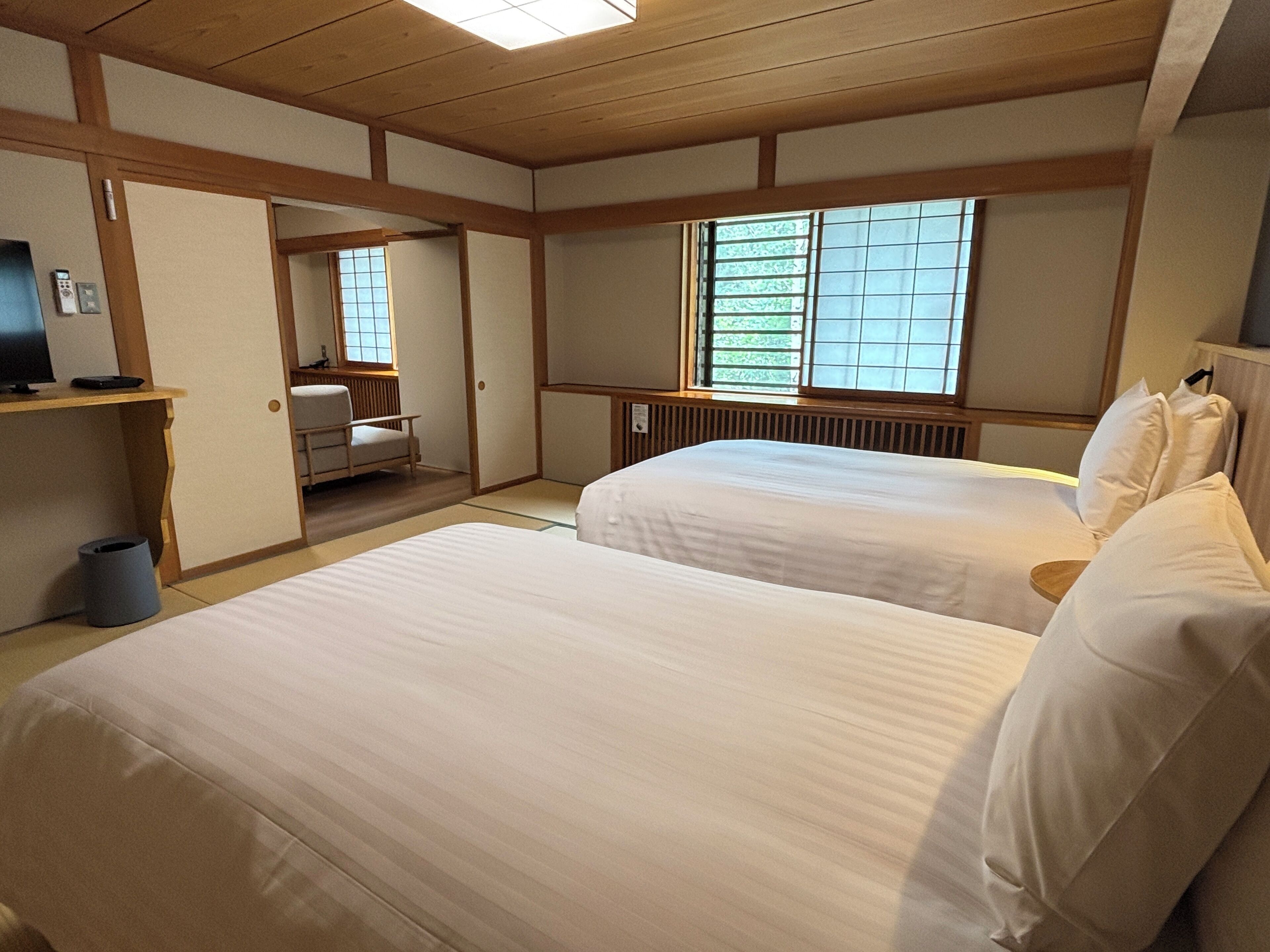 Habitación de hotel con dos camas, un escritorio con computadora, una silla y una ventana con persianas.