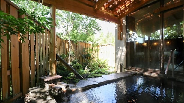 Ein Außenbereich mit Whirlpool, einer Holzterrasse, Steinstufen und einer Glaseinfassung.