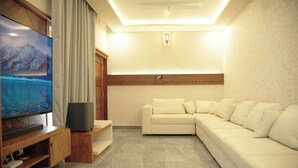 A modern living room with a flat-screen TV, a wooden entertainment unit, a white sofa, and a stone-tiled floor. - Gentur Enclave  (Mananthavady)