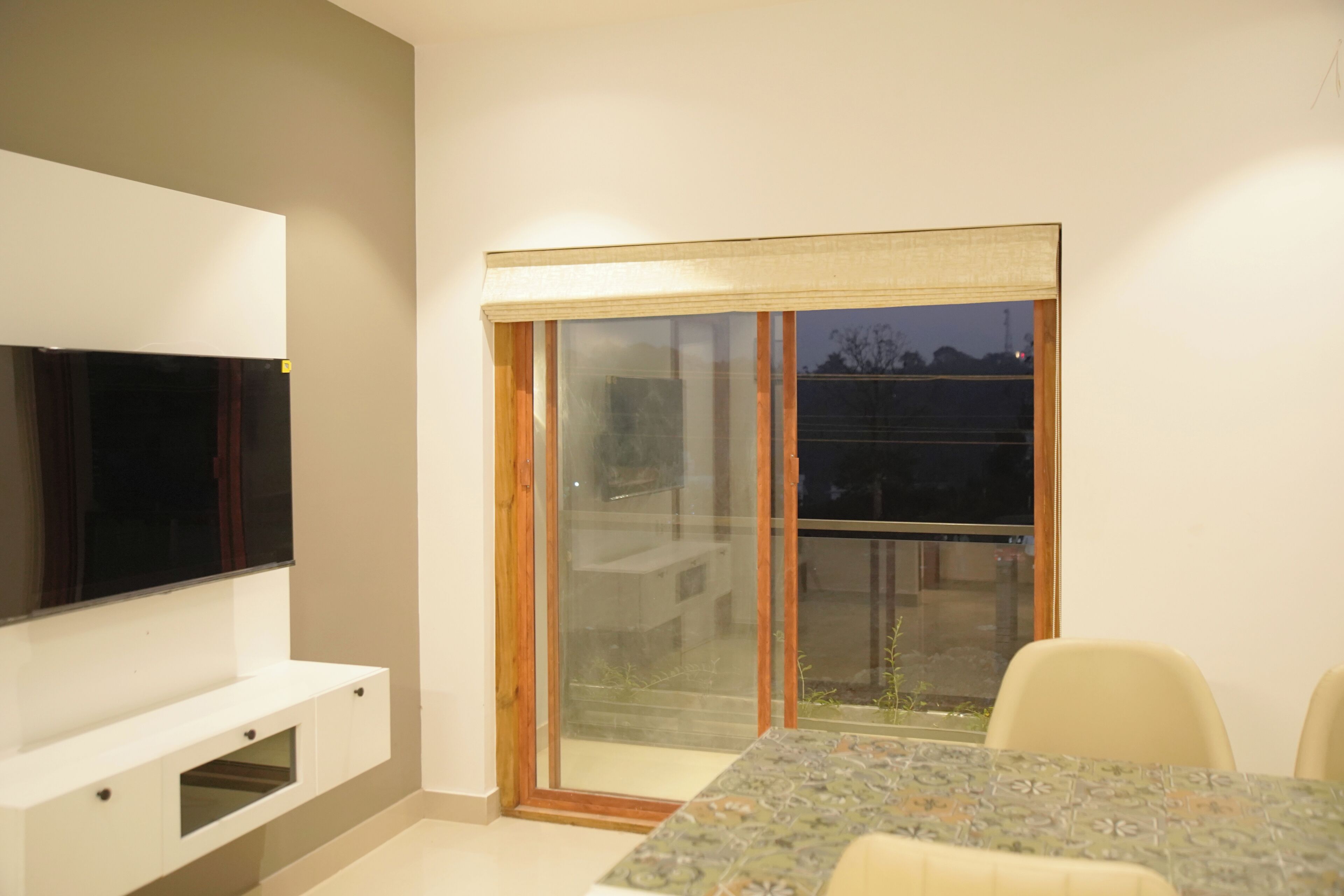 A modern living room with a flat-screen TV, a dining table with chairs, and a sliding glass door leading to an outdoor area.