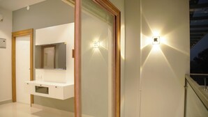 A modern bathroom with a white vanity, a mirror, and two wall-mounted lights. - Gentur Enclave  (Mananthavady)