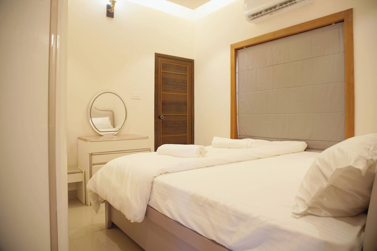 Un dormitorio con cama, mesita de noche, espejo y puerta.