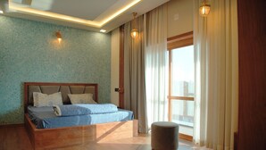 A modern bedroom with a wooden bed, a small ottoman, and a large window with curtains. - Gentur Enclave  (Mananthavady)