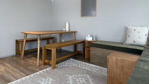 Quarto pequeno com escrivaninha de madeira, uma mesa, um banco, um sofá e um ar condicionado fixado na parede.