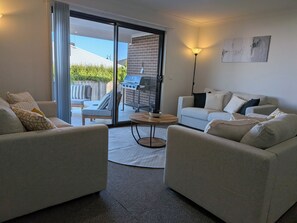 Ein modernes Wohnzimmer mit zwei Sofas, einem Couchtisch und einer Glasschiebetür, die auf eine Terrasse mit Grill führt.