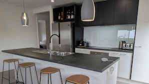 Une cuisine moderne dotée d’un îlot central, de tabourets de bar, d’un évier encastré et d’une machine à café.